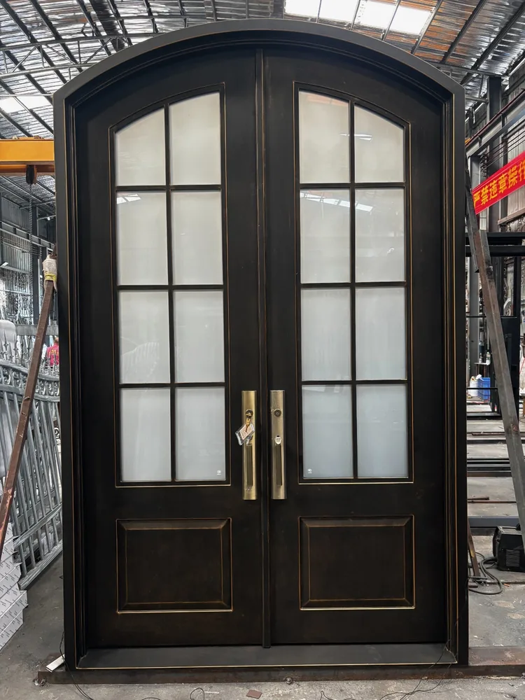 Arched dark bronze iron double doors with divided glass, standing in a workshop