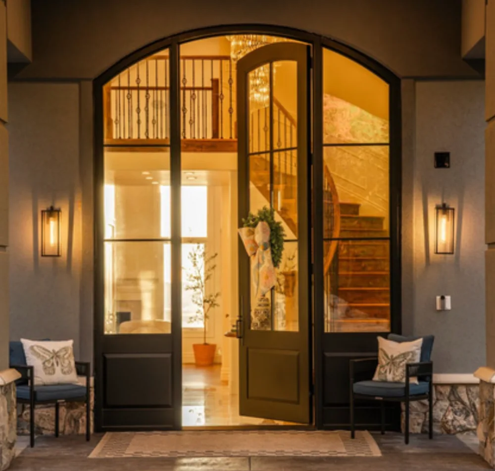 Arched black iron double entry doors with sidelites, one door open, at evening